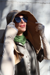 Woman wearing a beige Sun Safe hat that covers face and shoulders, sun safe gloves, sun safe neck scarf and sunglasses on.