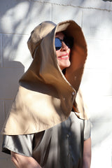 Woman wearing a beige Sun Safe hat clipped in the middle that covers face and shoulders with sunglasses on.